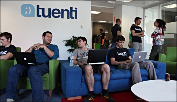 Vestíbulo de las oficinas de Tuenti en Madrid, varios informáticos sentados en sillones con sus ordenadores.